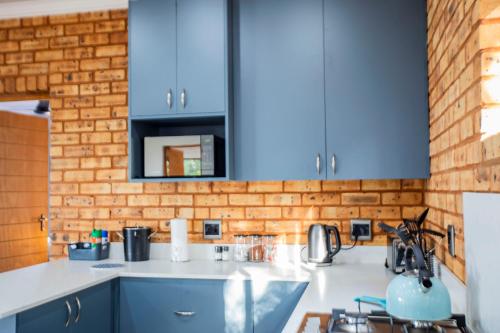 a kitchen with blue cabinets and a brick wall at Sink Huis at Benlize in Pelindaba