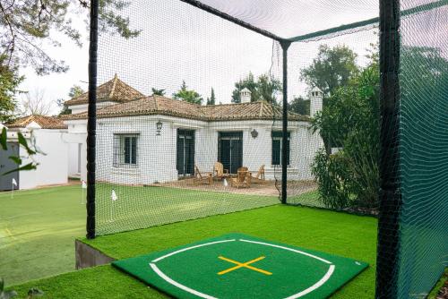 a tennis court with a batting cage with a house at La Pinta Golf Villa Sotogrande in Sotogrande