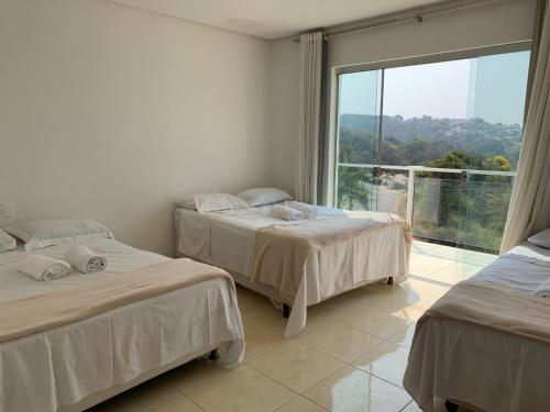 two beds in a room with a large window at Pousada Pontal de Escarpas in Capitólio