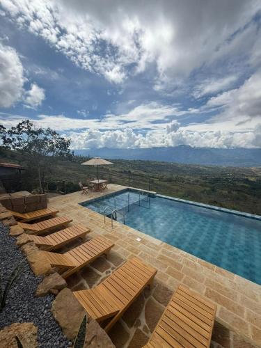 a swimming pool with benches and a view of the mountains at Hotel Cariguá in Barichara
