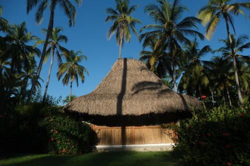 a straw hut with palm trees in the background at Hotel Playa Bonita Tayrona in Buritaca