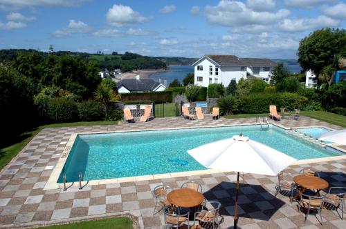 uma piscina com mesas e cadeiras e um guarda-sol em Merlewood Hotel em Saundersfoot