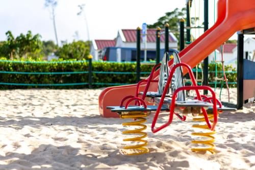 a playground with a red slide in the sand at Parque De Campismo Orbitur Gala in Figueira da Foz