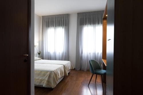a bedroom with a bed and a chair next to a window at Hotel Vienna in Marghera