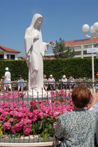 a woman taking a picture of a statue in a garden at Guest House OK in Međugorje