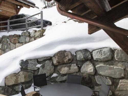 a stone wall with a table and chairs in the snow at Chalet in Les Masses with garden in Agettes