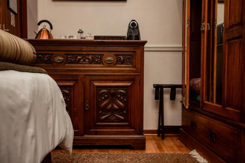 a wooden dresser in a bedroom next to a bed at Kleine Constantia Boutique Guest House in Roodepoort