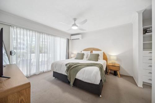 a white bedroom with a bed and a large window at Windsong Caloundra Sunsets Sea Breezes and Style in Caloundra