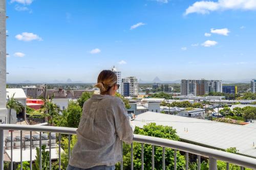 a woman standing on a balcony looking at the city at Windsong Caloundra Sunsets Sea Breezes and Style in Caloundra