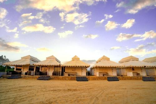 a group of buildings with roofs on a dirt field at Khamma Ghani Resort with pool Luxury camp in Jaisalmer in Jaisalmer
