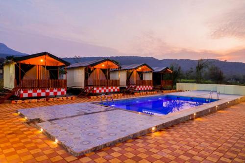 una grande piscina con un gruppo di capanne di Publiq Darbar Tent House a Pune