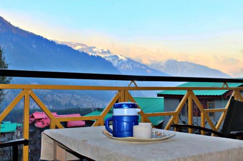 a table with a blue thermos on top of a balcony with mountains at Apple Field House in Manāli