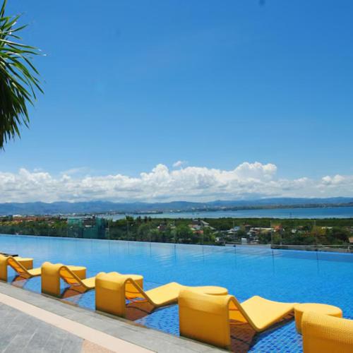 a large swimming pool with yellow lounge chairs at Mactan Newtown 8 Boulevard Deluxe Ocean View in Lapu Lapu City