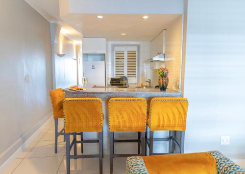 a kitchen with a bar with orange bar stools at Peninsula All Suite Hotel by Dream Resorts in Cape Town