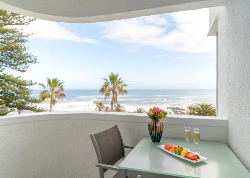 a table with a bowl of fruit and two glasses of wine at Peninsula All Suite Hotel by Dream Resorts in Cape Town