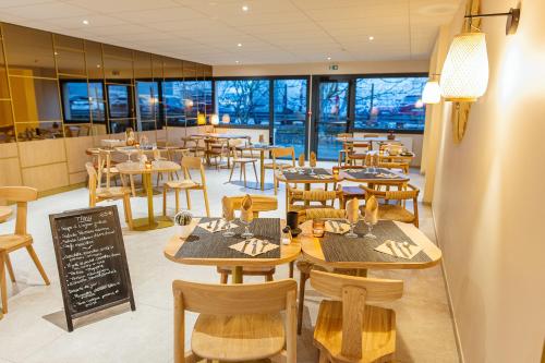 a restaurant with wooden tables and chairs and windows at Hotel Bhoma Troyes in Troyes