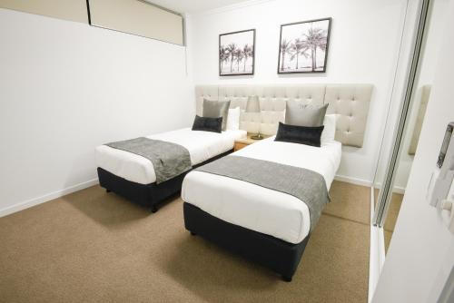 two beds in a room with white walls at Pacific Sands Apartments Mackay in Mackay