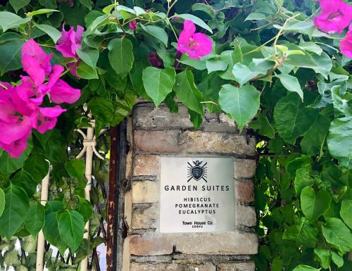 a sign on a brick wall with pink flowers at Garden Suites in Corfu