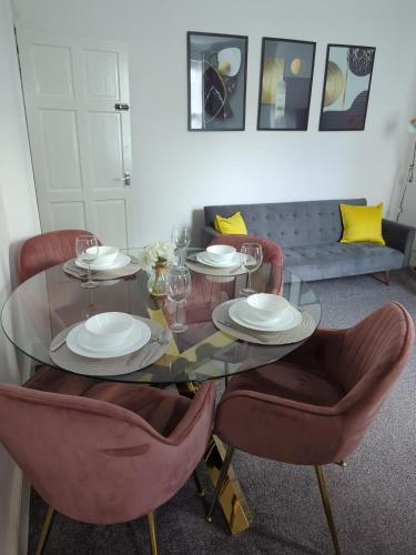 a glass table with chairs and plates and glasses on it at Charming 3-Bedroom House - Prime Location in Wolverhampton! in Wolverhampton