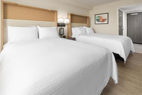 two beds in a hotel room with white sheets at Holiday Inn & Suites Richmond West End by IHG in Richmond