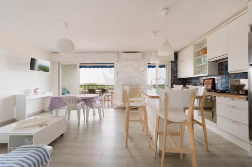 - une cuisine et une salle à manger avec des armoires et des chaises blanches dans l'établissement AS13357 - P3 face à la plage sans route à traverser, proche centre ville avec parking privé, au Grau-du-Roi