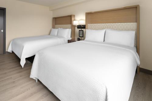 two beds in a hotel room with white sheets at Holiday Inn & Suites Richmond West End by IHG in Richmond