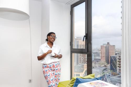 a woman standing in a window looking at a cell phone at Seen Hotel Abidjan Plateau in Abidjan