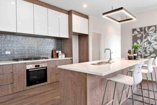a kitchen with white cabinets and a kitchen island with stools at Modern Beach Retreat 4 bedrooms in Papamoa