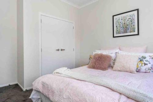 a white bedroom with a bed with pink blankets and pillows at Modern Beach Retreat 4 bedrooms in Papamoa