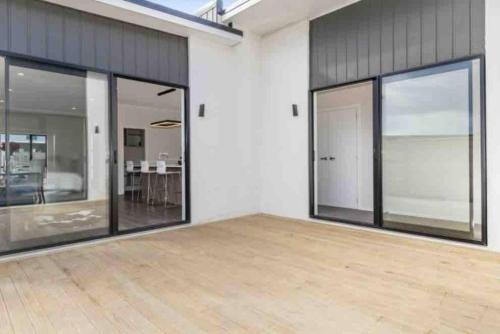 an empty room with large windows and a wooden floor at Modern Beach Retreat 4 bedrooms in Papamoa