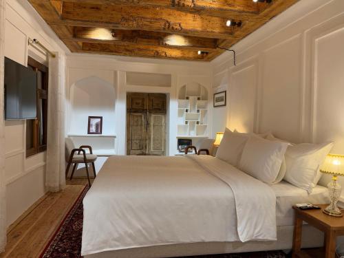 a bedroom with a white bed with a wooden ceiling at Usman Heritage in Bukhara