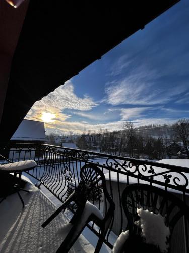 a snow covered balcony with two benches and the sunset at Pokoje z własnymi aneksami kuchennymi - Zbigniew Lassak in Biały Dunajec