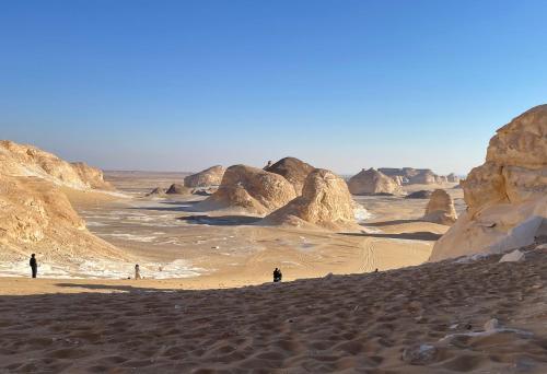 people walking in a desert with rocks in the background at Ahmed Safari Camp in Bawiti