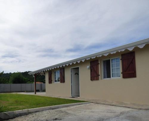 a house with brown shuttered windows and a driveway at Villa avec piscine privée au Vauclin in Le Vauclin