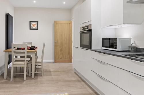 a kitchen with white cabinets and a table with chairs at The Heart of Brixham, Bolton Plaice, Luxury Apartment in Brixham