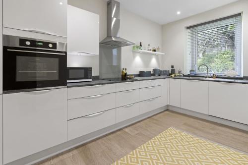 a kitchen with white cabinets and a black appliance at The Heart of Brixham, Bolton Plaice, Luxury Apartment in Brixham