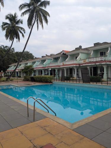 a swimming pool in front of a building with a palm tree at Cozy Cabana - The Perfect Getaway in Benaulim
