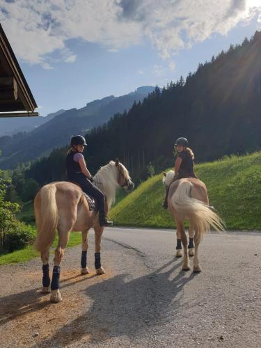 two people are riding horses on a road at Hinterjetzbachhof in Maria Alm am Steinernen Meer