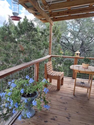 a wooden deck with a bench and a table and blue flowers at Boulderdash Birdhouse Studio in Bandera