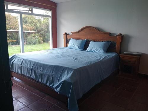 a bedroom with a bed with blue sheets and a window at La Juana Posada Campesina in Tenjo