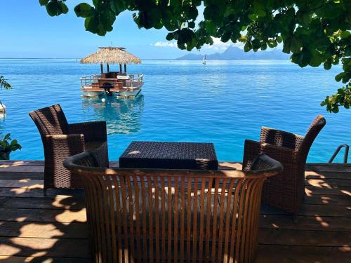 a table and chairs with a boat in the water at Moana Waterfront Bungalow in Punaauia