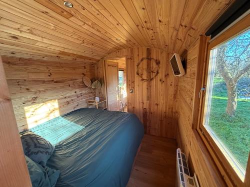 una cama en una cabaña de troncos con ventana en La Roulotte Saintaise, en Saintes