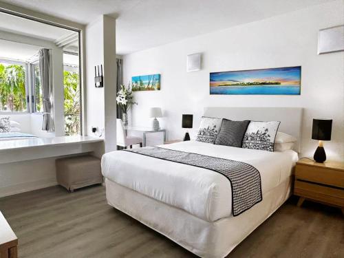 a white bedroom with a large bed and a window at Palm Cove Beachside Apartments - Sea and Mountain Views in Palm Cove