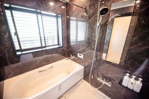 a bathroom with a tub and a shower with a window at Ocean Front Villa Katsuura やどかり in Kawazu