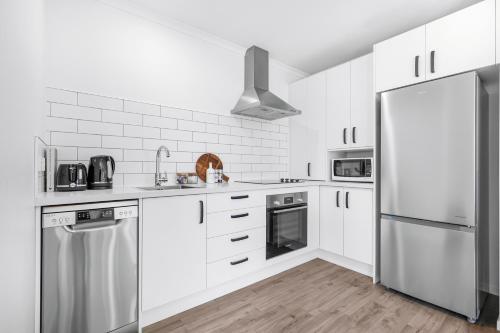 a white kitchen with white cabinets and a refrigerator at Stylish, Modern and Central in Hamilton