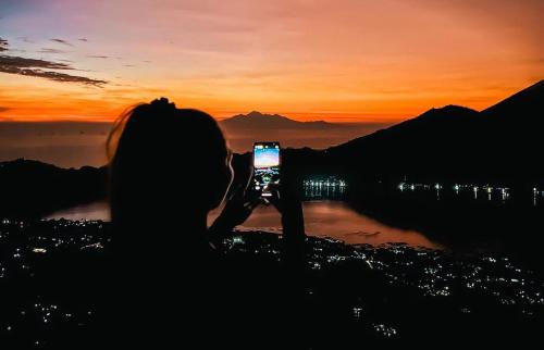 a woman taking a picture of the sunset with her cell phone at The Indria Point in Kintamani