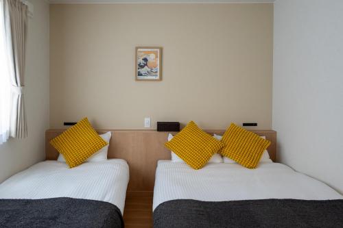two beds in a room with yellow pillows on them at TKD HOUSE Furano 2 in Furano
