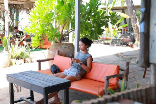 a woman sitting on an orange couch looking at her cell phone at EVA HUT Mui Ne Beach Hostel in Mui Ne