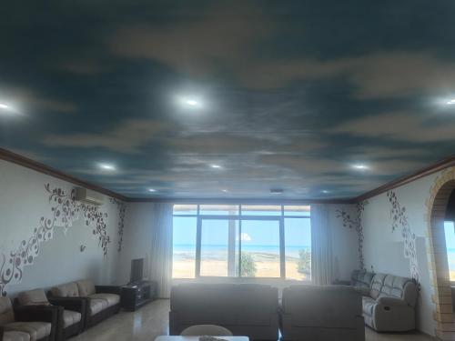 a living room with couches and a large window at NatureLand Beach Villa in Ḩabshān