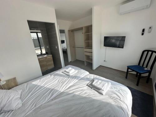 - un lit blanc dans une chambre avec une chaise et une télévision dans l'établissement Maison 90 avec 8 chambres lechaffardcom, à Satolas-et-Bonce